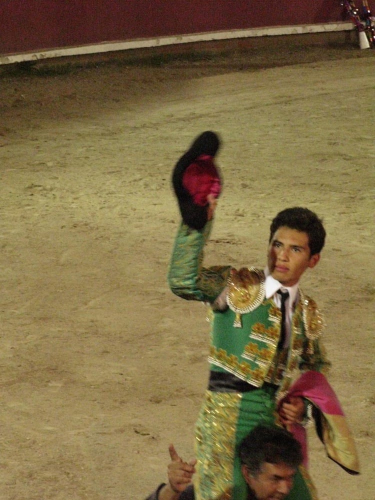 Francisco Martinez salutes the crowd as he rides out of the bullring on the shoulders of another man. Judges award a bullfighter a salida en hombros (literally “exit on shoulders”) if he performs exceptionally well.
