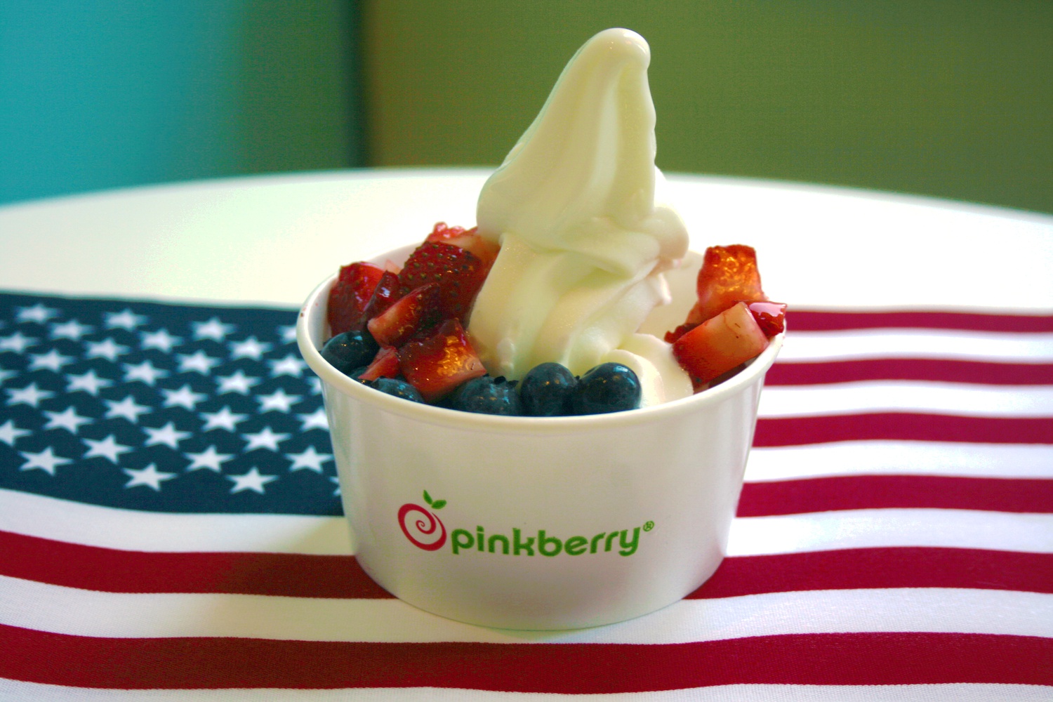 A small red, white, and blue Pinkberry sits upon the red, white, and blue.