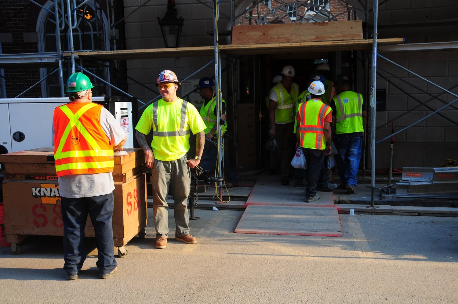 Workers talk near and walk through a Mill Street entrance to Old Leverett at around 6:30 p.m. Friday. Temperatures were still around 90 degrees in the area as they wrapped up the day's electrical and demolition work.