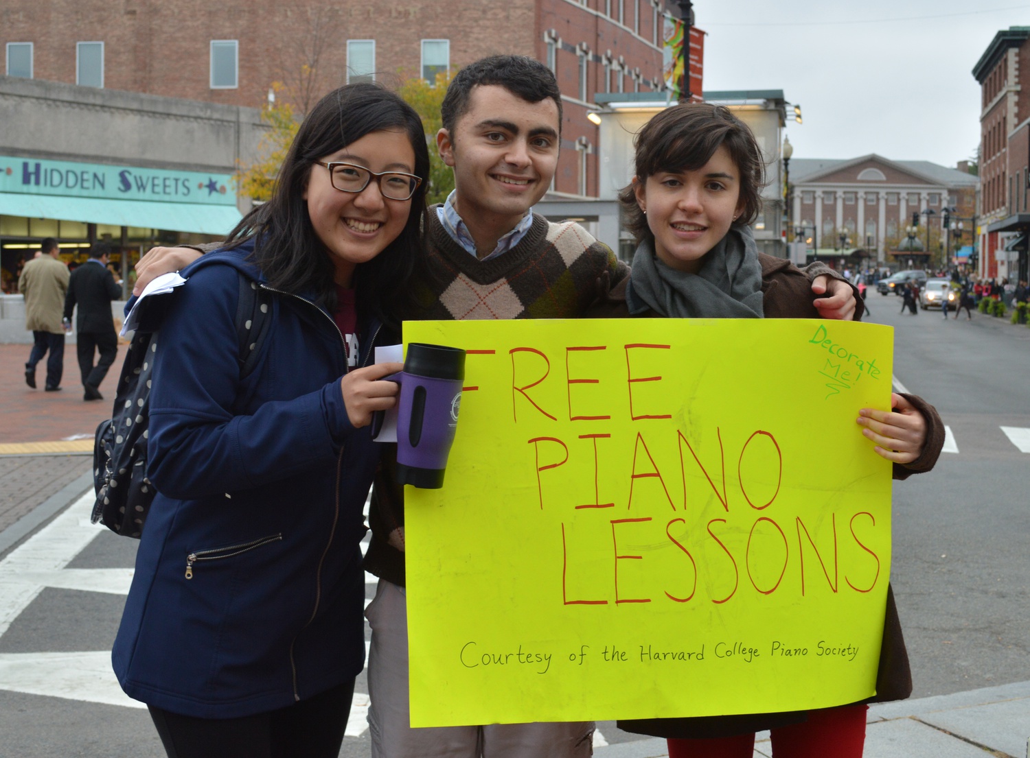 Tania Rivers-Moore, Cherie Hu, and Amir Bitran hold up a sign on Saturday afternoon in Brattle Square.