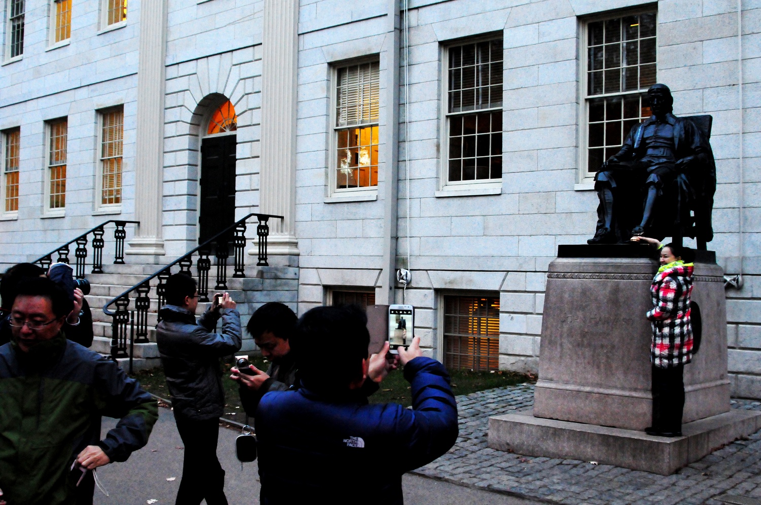 Tourists take pictures with the most famous college statue in the world on a cold Tuesday afternoon.  A tourist touches the foot of the statue, which is supposed to bring good luck. Harvard students know otherwise.  