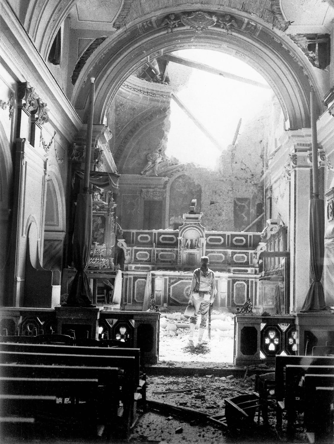 A private enters a bombed-out cathedral in Acerno, Italy, during WWII.