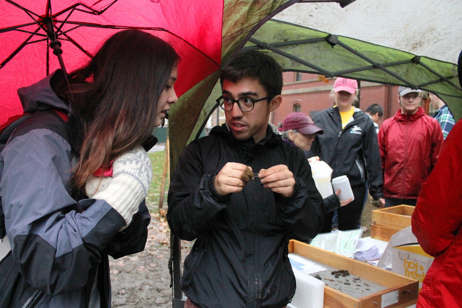 Santiago Pardo '16, member of the Harvard Yard Archaeology Project, explains recent finds to Hannah K. Rasmussen '16 outside of Matthews Hall despite the rain and cold weather on Thursday afternoon. 