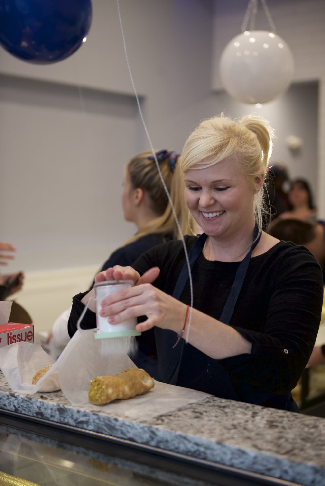 Danielle R Papa, the manager of the Cambridge location of Mike's Pastry, sprinkles powdered sugar on two cannoli for a customer. Mike's Pastry opened in Harvard Square on Thursday and is open seven days a week from 8am to 10pm.