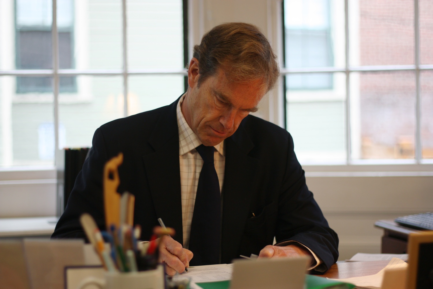 Dean of Freshmen Tom Dingman signs an extended eligibility form for a student-athlete at his desk.
