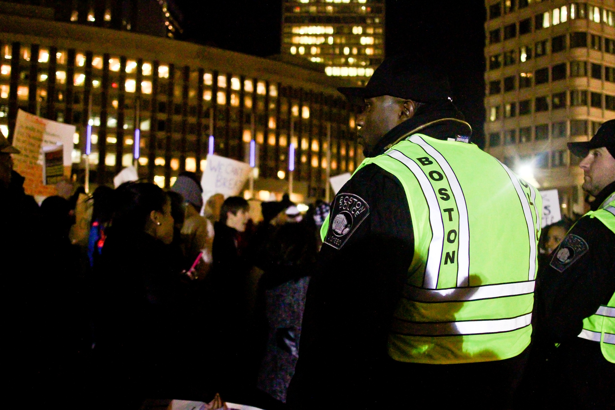 Police officers stand on guard at the Government Center as protesters stream by.