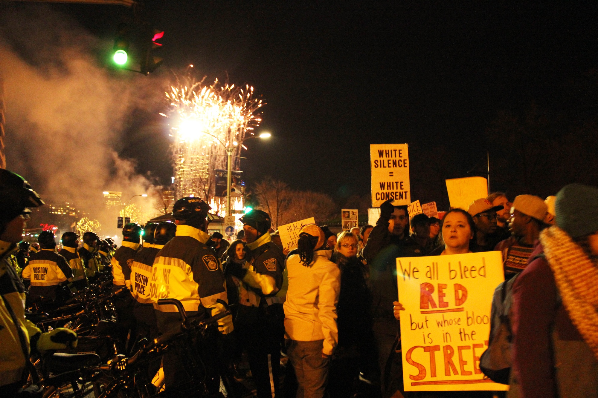 Fireworks from the Boston Common tree lighting ceremony go off as police and protestors alike gather in the streets.