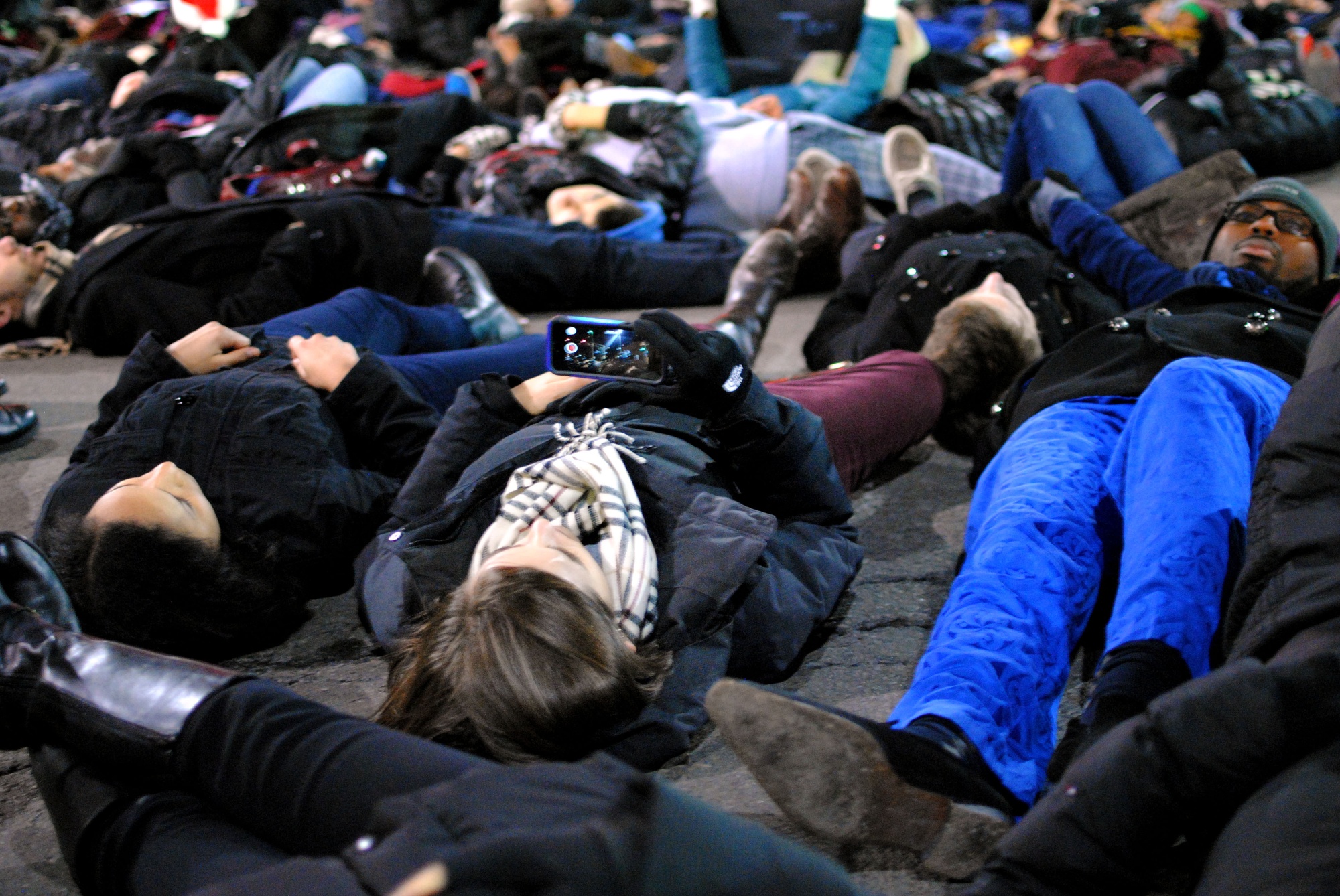 A protestor takes a photo during a die-in in Central Square on Friday evening as a part of the 'March on Harvard' protest. 