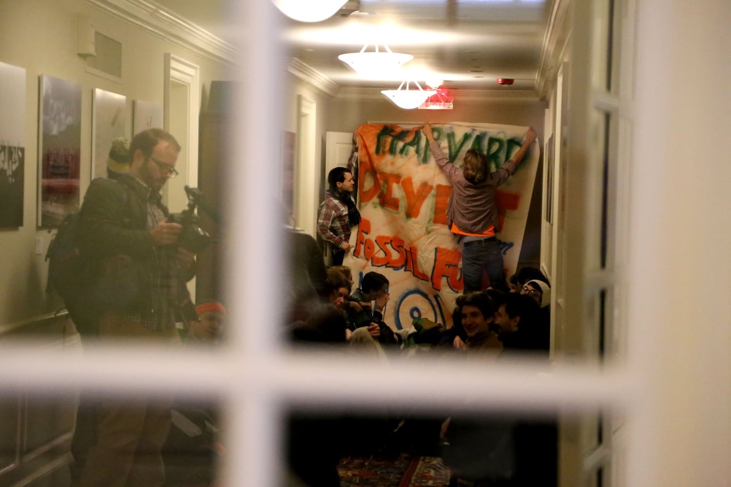 Canyon S. Woodward '15 of Divest Harvard hangs a banner during a protest in Massachusetts Hall. A group of students rushed into the building that houses the University president's office this morning.