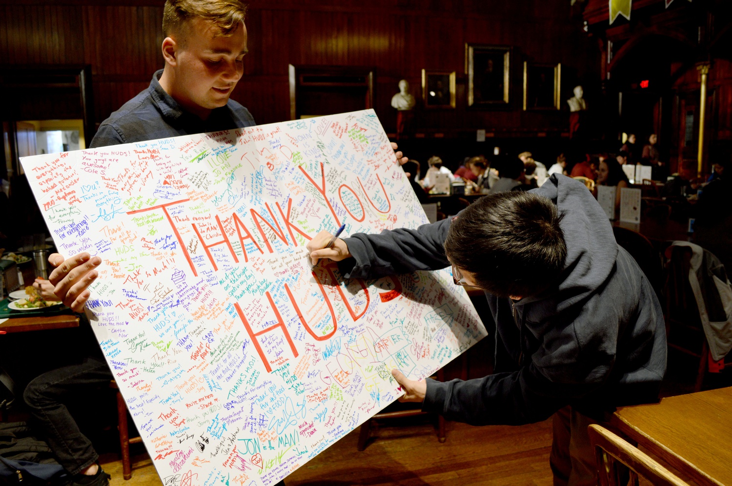 Undergraduate Council representative Wyatt M. Robertson '18 holds a 'Thank You' poster for HUDS staff as Moses Kim '18 signs.  The UC organized the 'HUDSy BERGday' event to express gratitude to the staff of Annenberg on behalf of the freshman class.