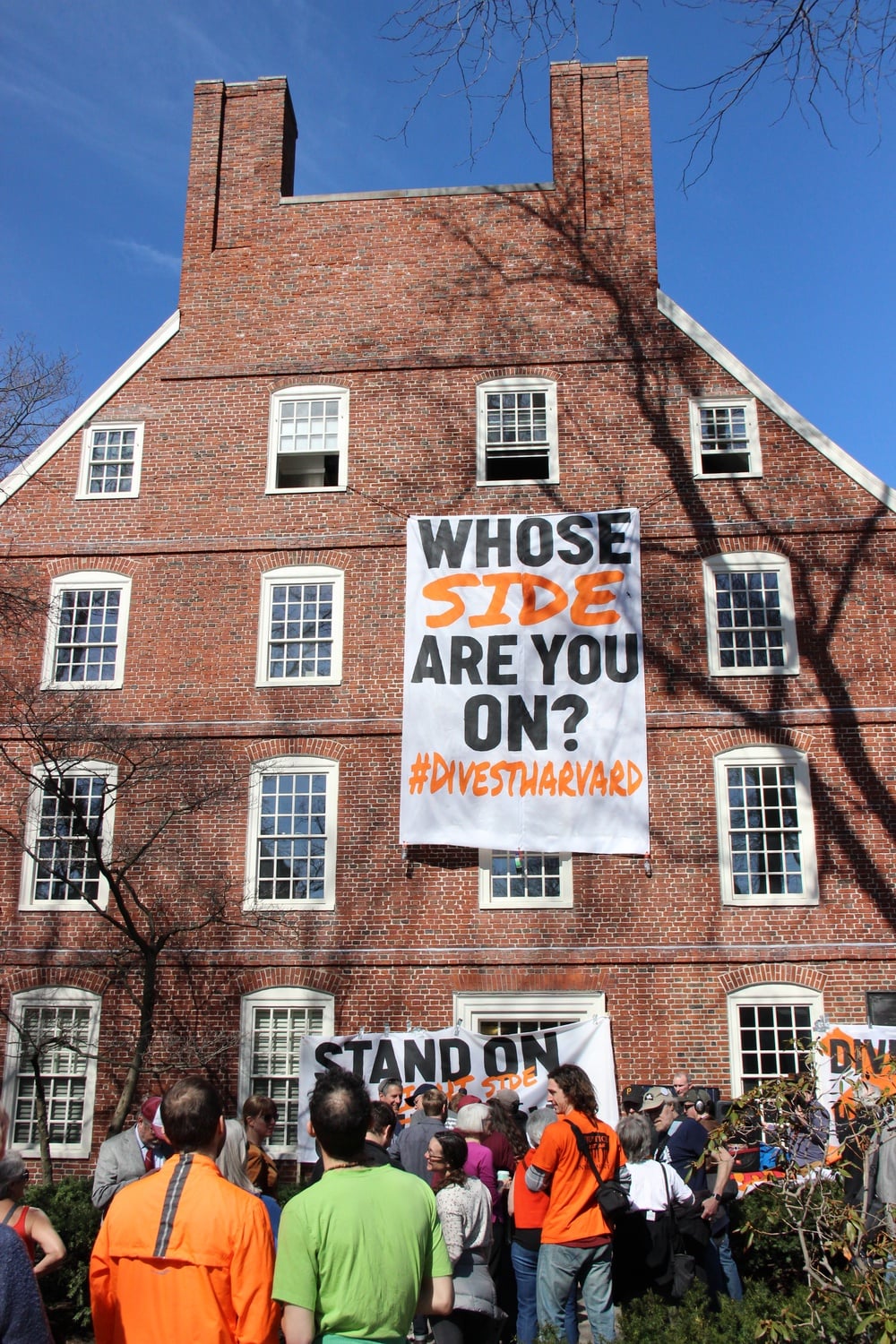 Protesters hang a banner from the upper floors of Massachusetts Hall. They held a kickoff rally Monday morning as part of "Harvard Heat Week."