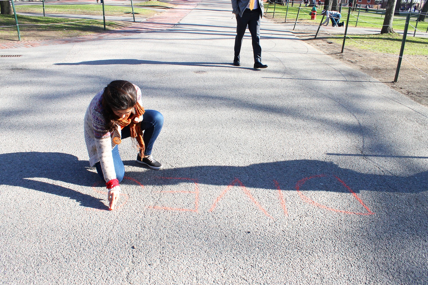 Sima Atri, a Harvard Law School student, writes "DIVEST” in chalk in Harvard Yard on Monday morning.