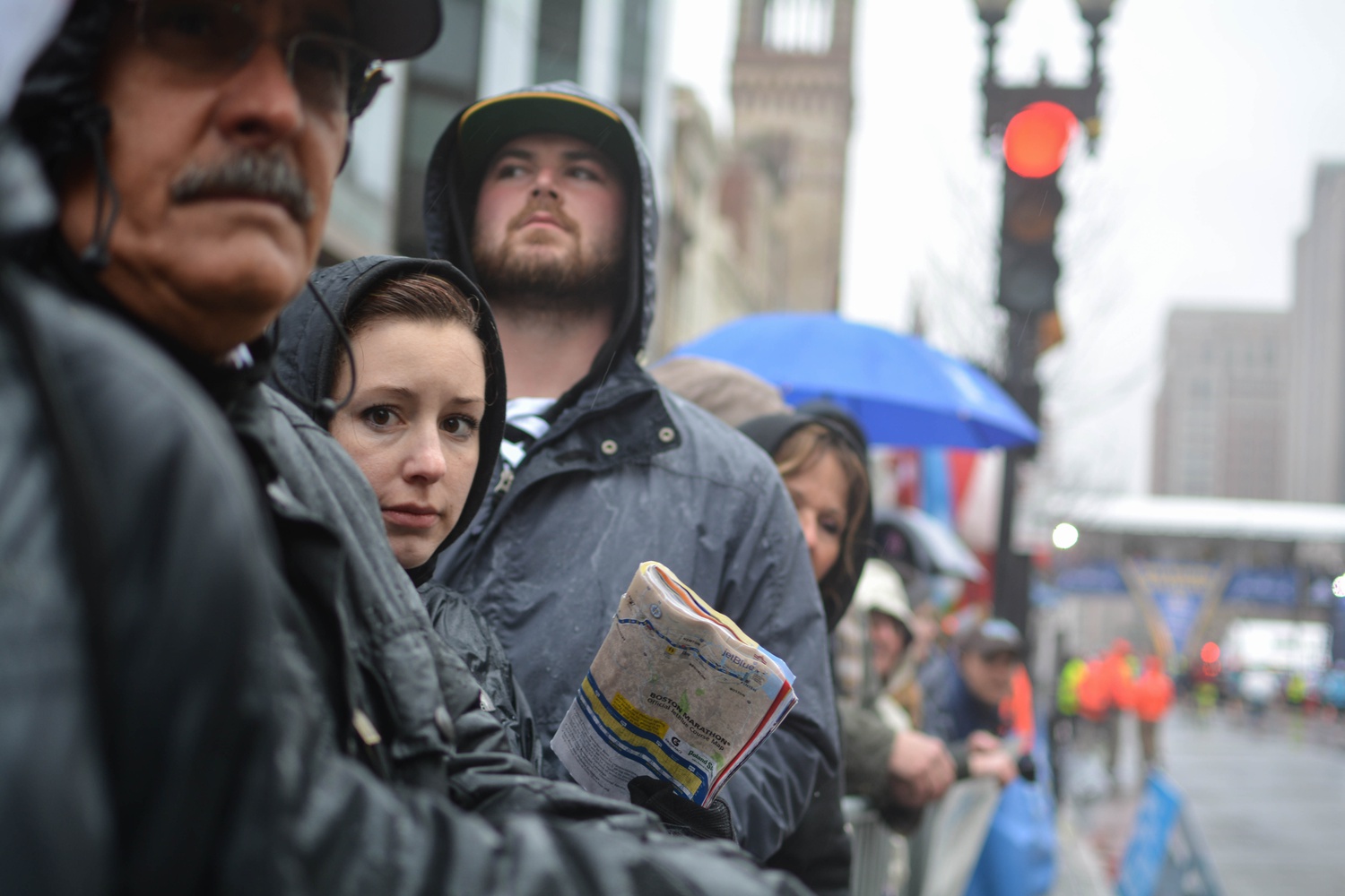 Spectators, lined along the finishing stretch of the marathon in Copley Square, stare down the road in anticipation. 
