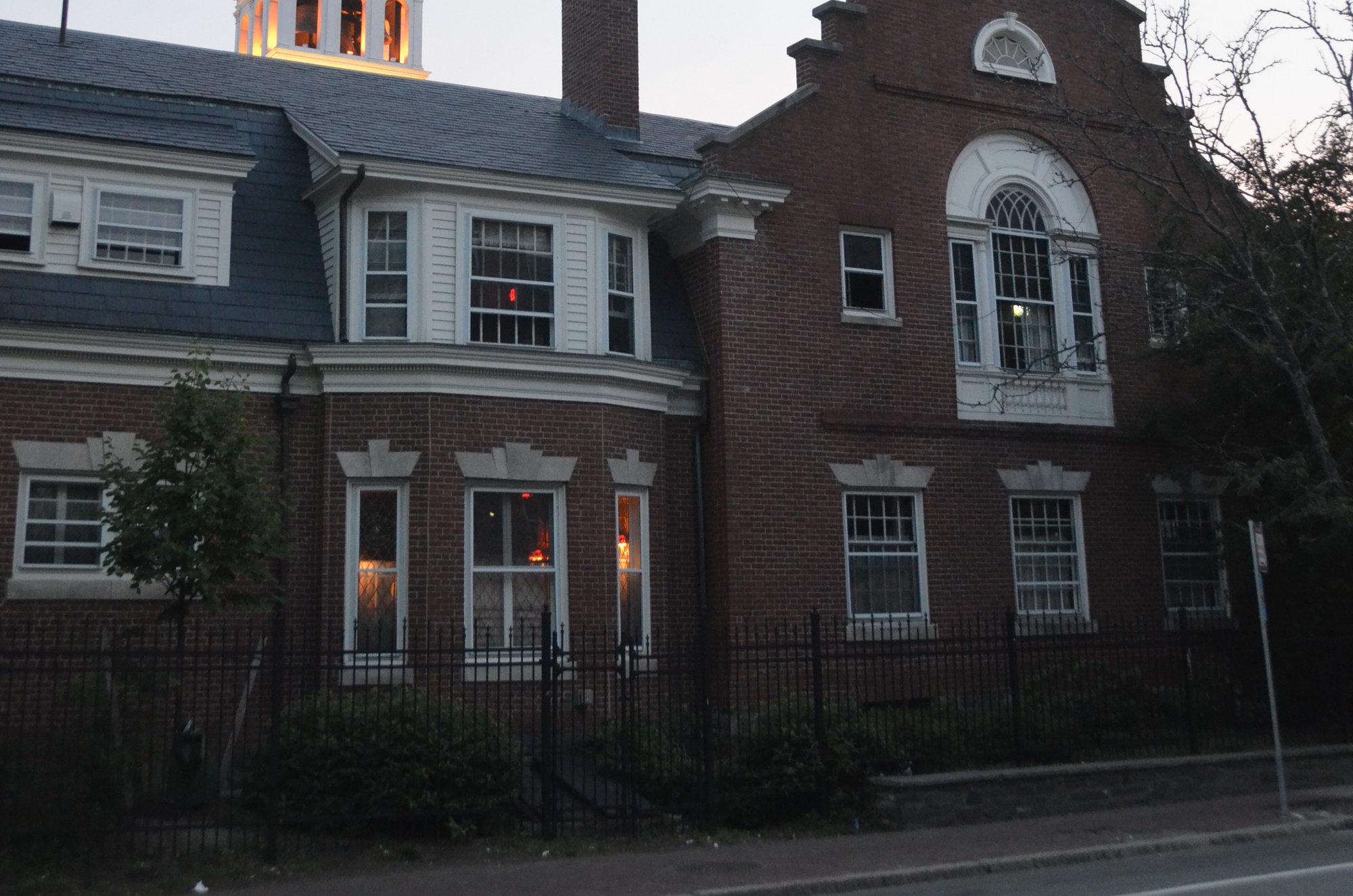 A glowing Lowell House Bell Tower peeks out above the roof of all-male final club The Fly on Monday evening.