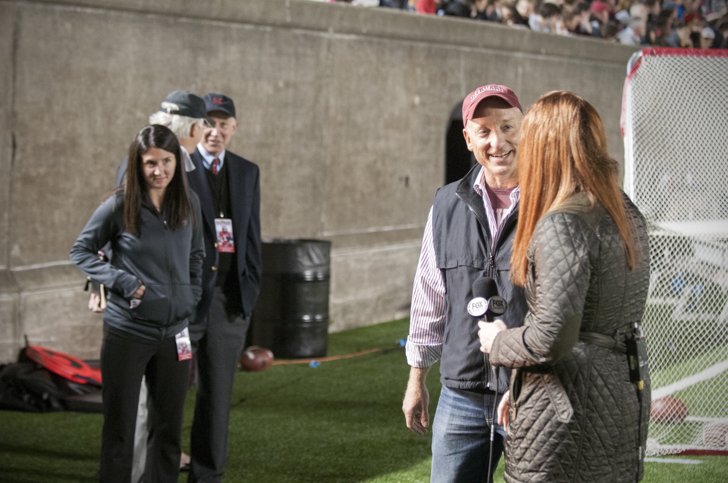 Associate Director of Athletic Communications Allison Miller, left, watches as Dean of the Faculty of Arts and Sciences Mike Smith is interviewed by a reporter from Fox College Sports. 