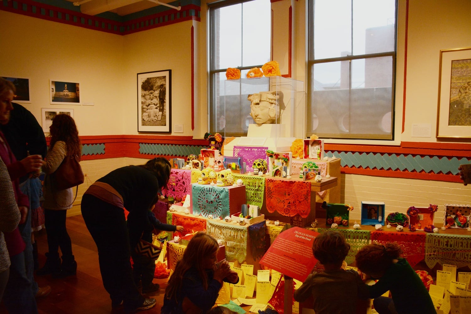 Peabody Museum visitors examine a table full of objects associated with the Day of the Dead.  This setup is part of the Peabody Museum's celebration of the Day of the Dead for local families.  