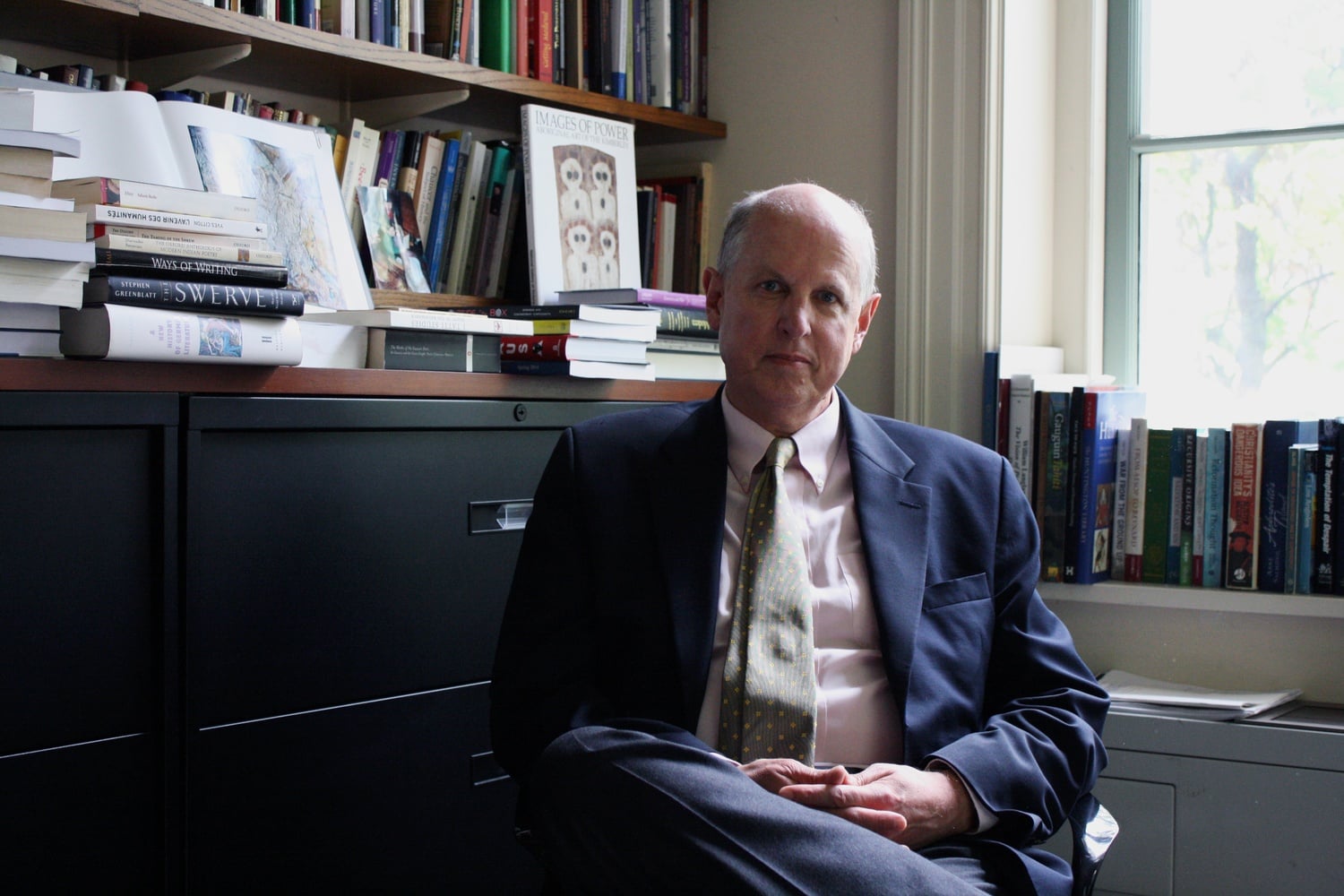 Professor James Simpson, Chair of the English Department, sits in front of a full wall of books in his office in the Barker Center.
