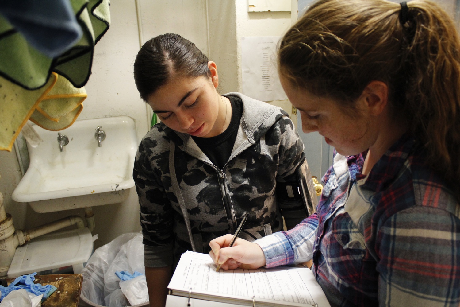 Sarah Lagan ‘19 and Noemi Valdez ‘19 look over a work hour log-in sheet in a Cabot House storage room. The two did Dorm Crew Fall Clean-Up together and continued to work as a team after finding that they were good partners. 