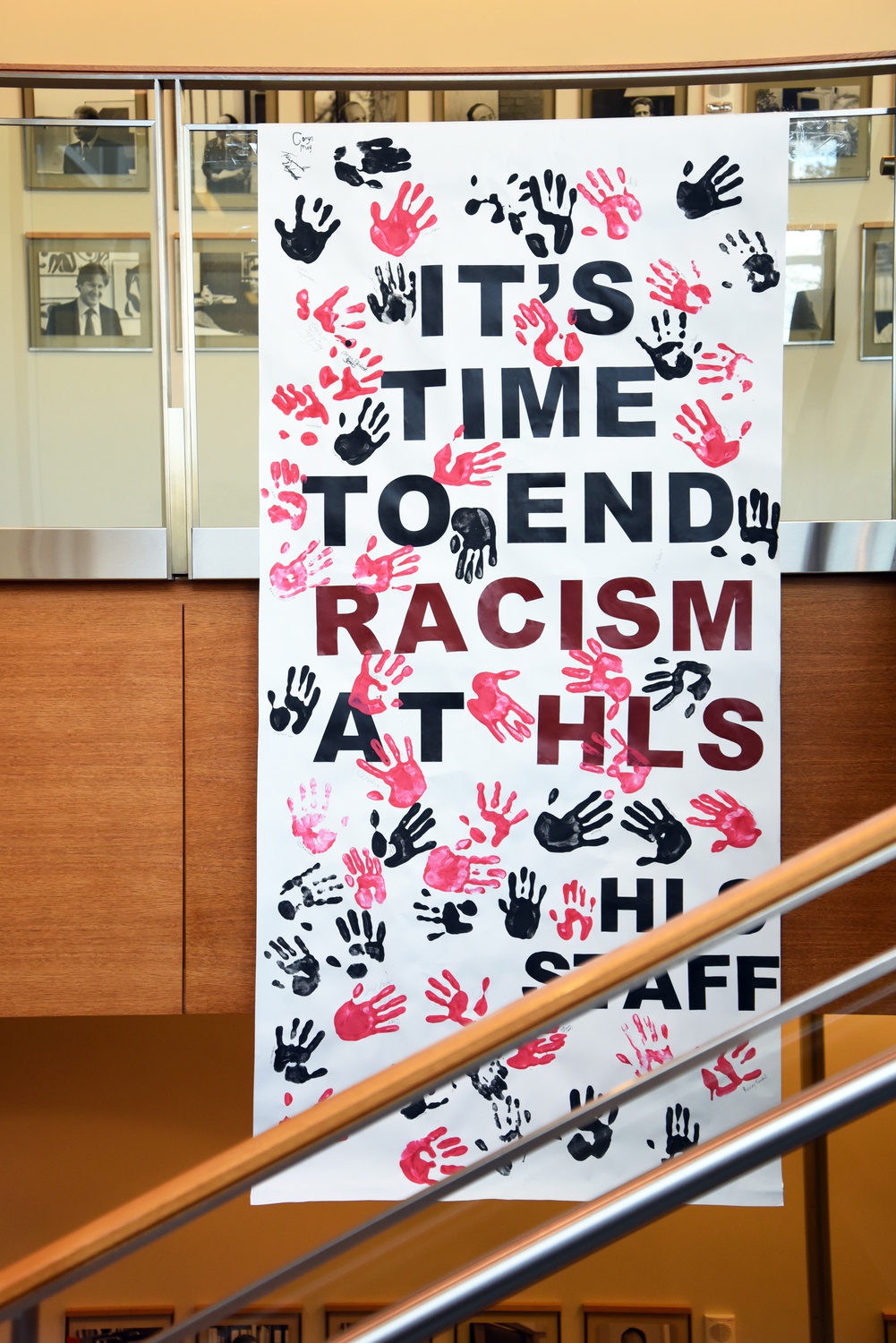 A sign reading “IT’S TIME TO END RACISM AT HLS,” signed “HLS STAFF,” hangs right above the portraits of black law professors that had been defaced with black tape in November.