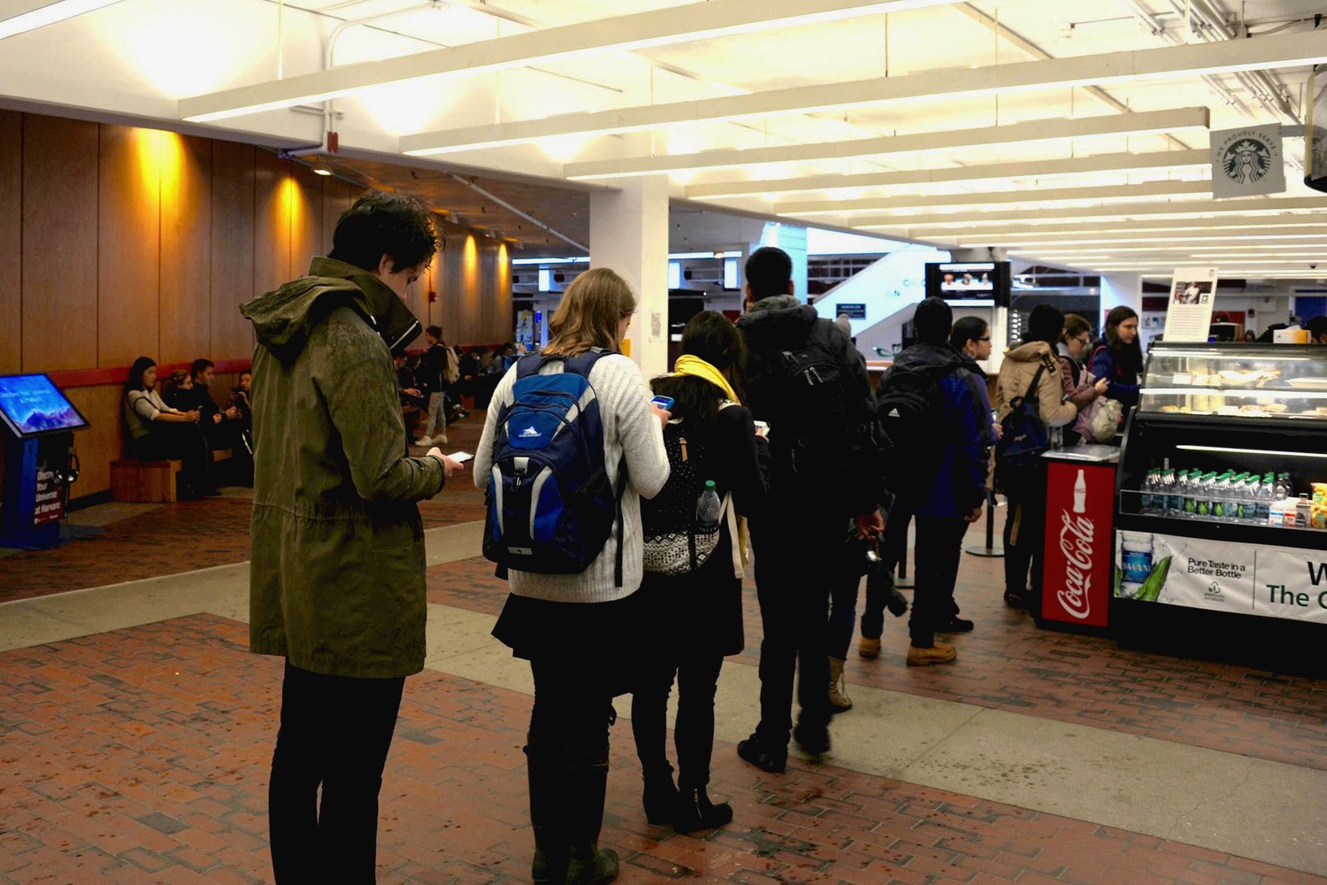 James R. O. Nakajima '18, left, checks Snapchat as he waits in line at the Greenhouse Cafe. Many Houses and campus spaces--from Annenberg Hall to Widener Library--recently created geotag filters on the app.