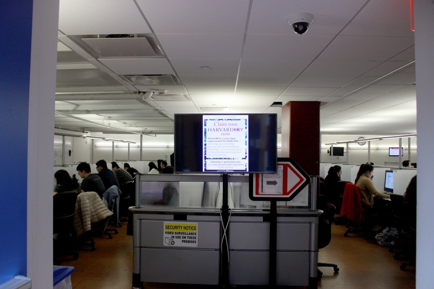 Students work in the HUIT Walk-in Help Center in the Science Center basement as a notice about the HarvardKey authentication system flashes onscreen.