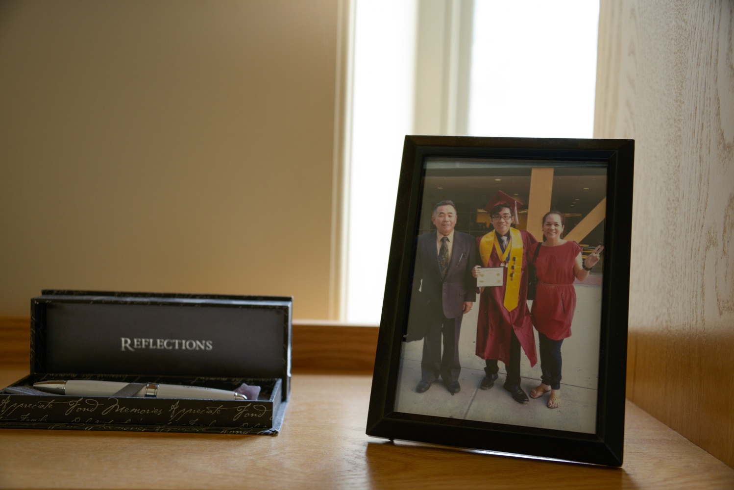 Daishi keeps memories of home, including a graduation photo with his parents and a pen, on his desk. 