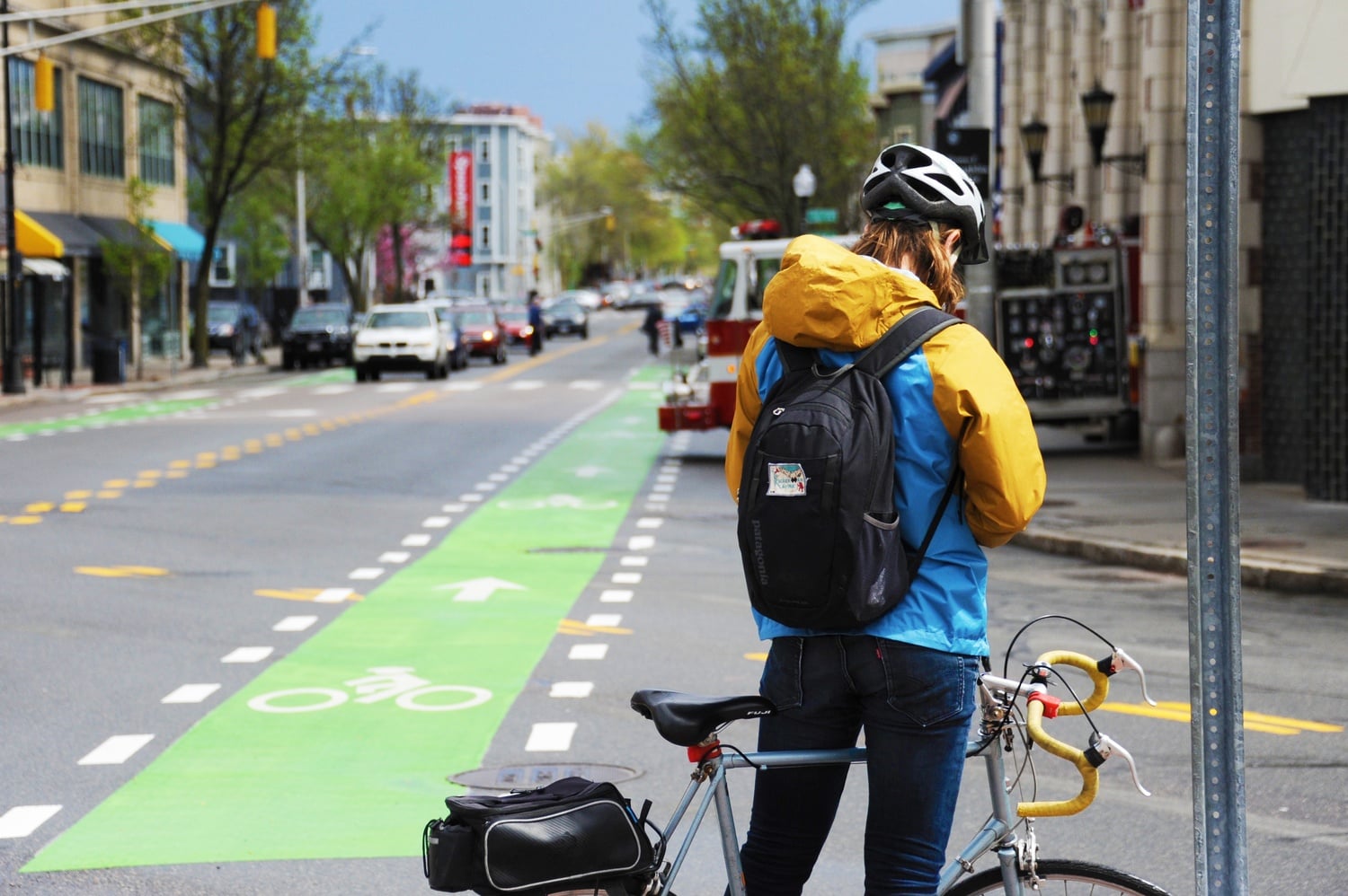 A bicyclist stands at the intersection of Cambridge St and Hampshire St, in Inman Square.