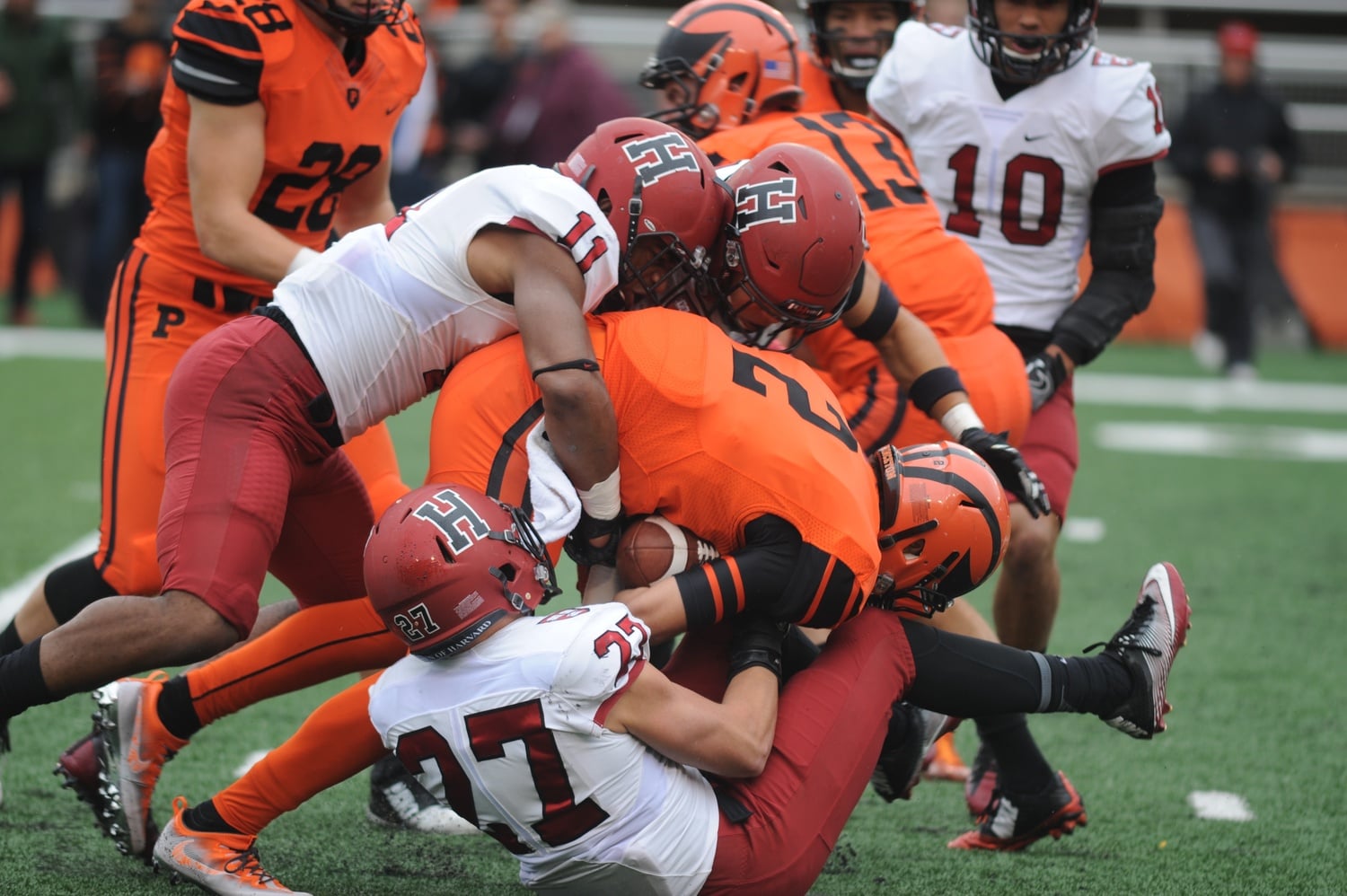 A trio of Crimson defenders, led  by senior Kolbi Brown (11), wraps up Princeton’s James Frusciante in a 23-20 Harvard overtime victory.