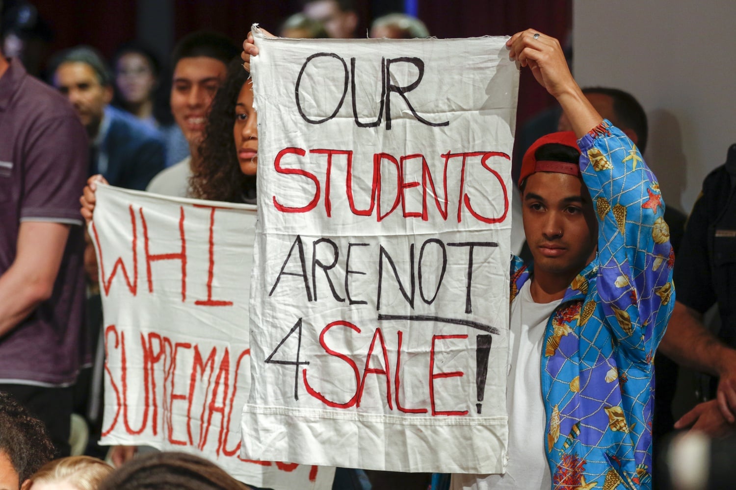 A student holds a banner protesting Secretary of Education Betsy DeVos' appearance at the Kennedy School Thursday evening. Some students silently disrupted the event indoors, while others rallied and chanted outdoors.