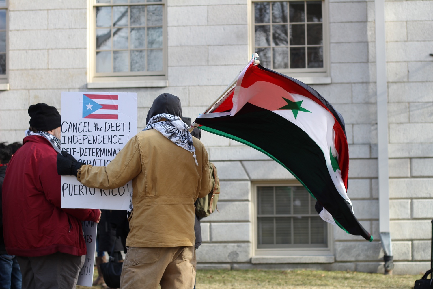 A protestor waves the Syrian national flag while carrying a sign for the "Stand With Puerto Rico" protest Wednesday afternoon.