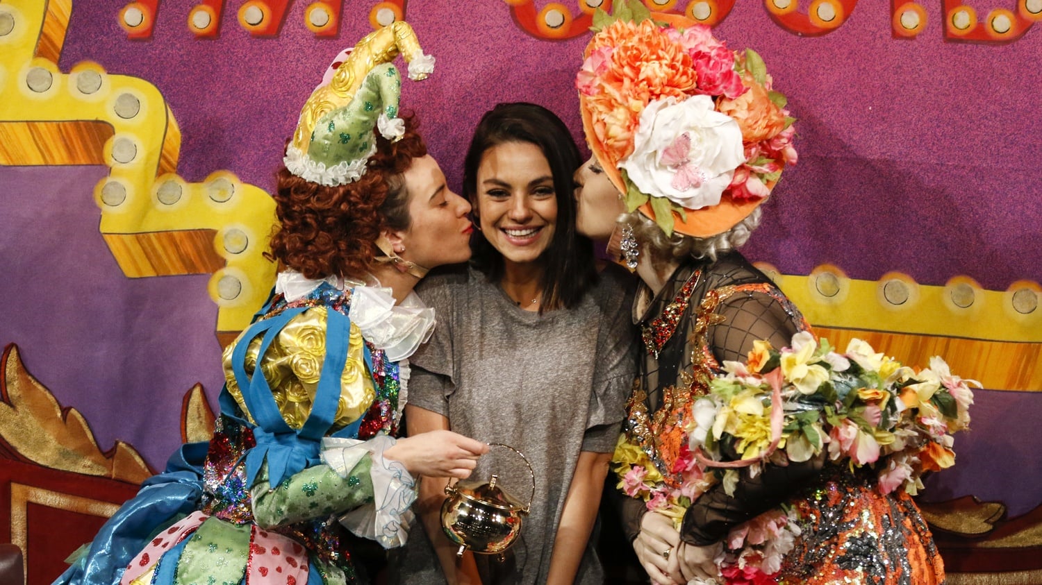 Hasty Pudding 2018 Woman of the Year Mila Kunis receives kisses from two Pudding cast members.