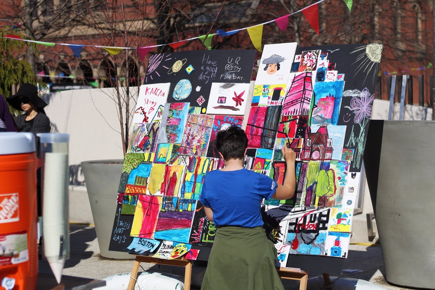 A student donning a blue Arts First t-shirt adds painting to a communal art display. Arts First is Harvard's annual art festival dedicated to promoting the arts.