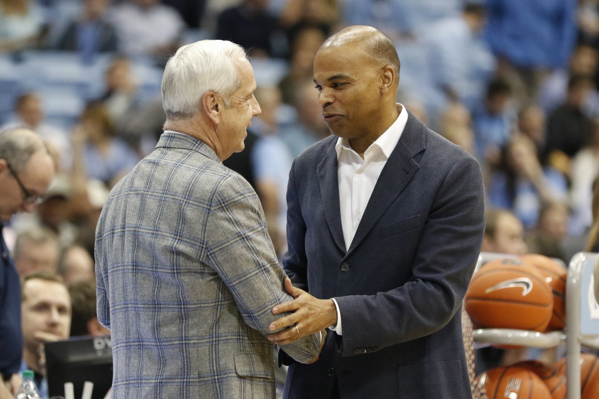 Coach Tommy Amaker and coaching legend Roy Williams embrace prior to the start of a game.