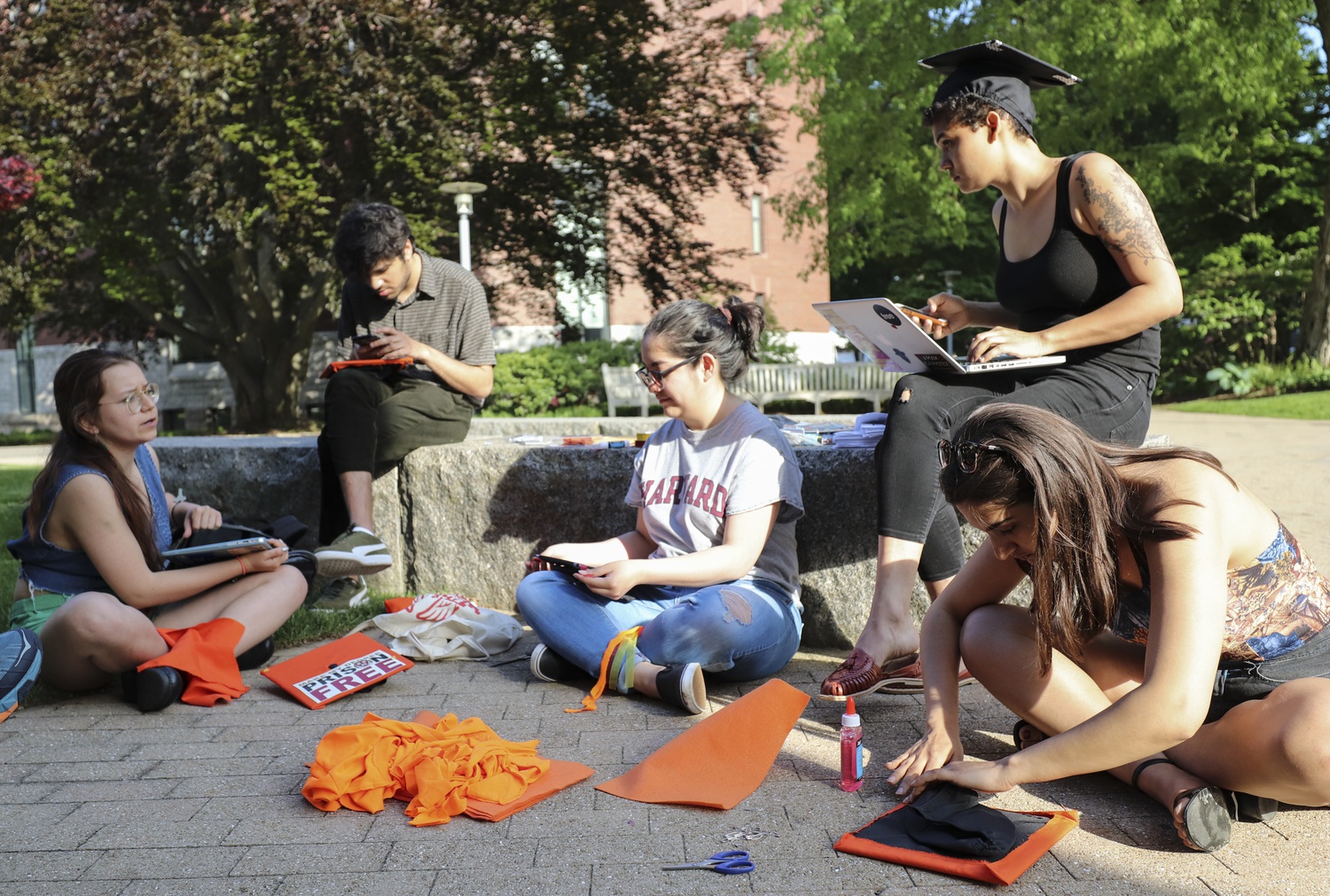 Members of Divest Harvard and the Harvard Prison Divestment Campaign decorate their graduation caps with orange cloth and felt outside the Casper Student Center Monday evening. Orange is the color of the fossil fuel divestment movement.