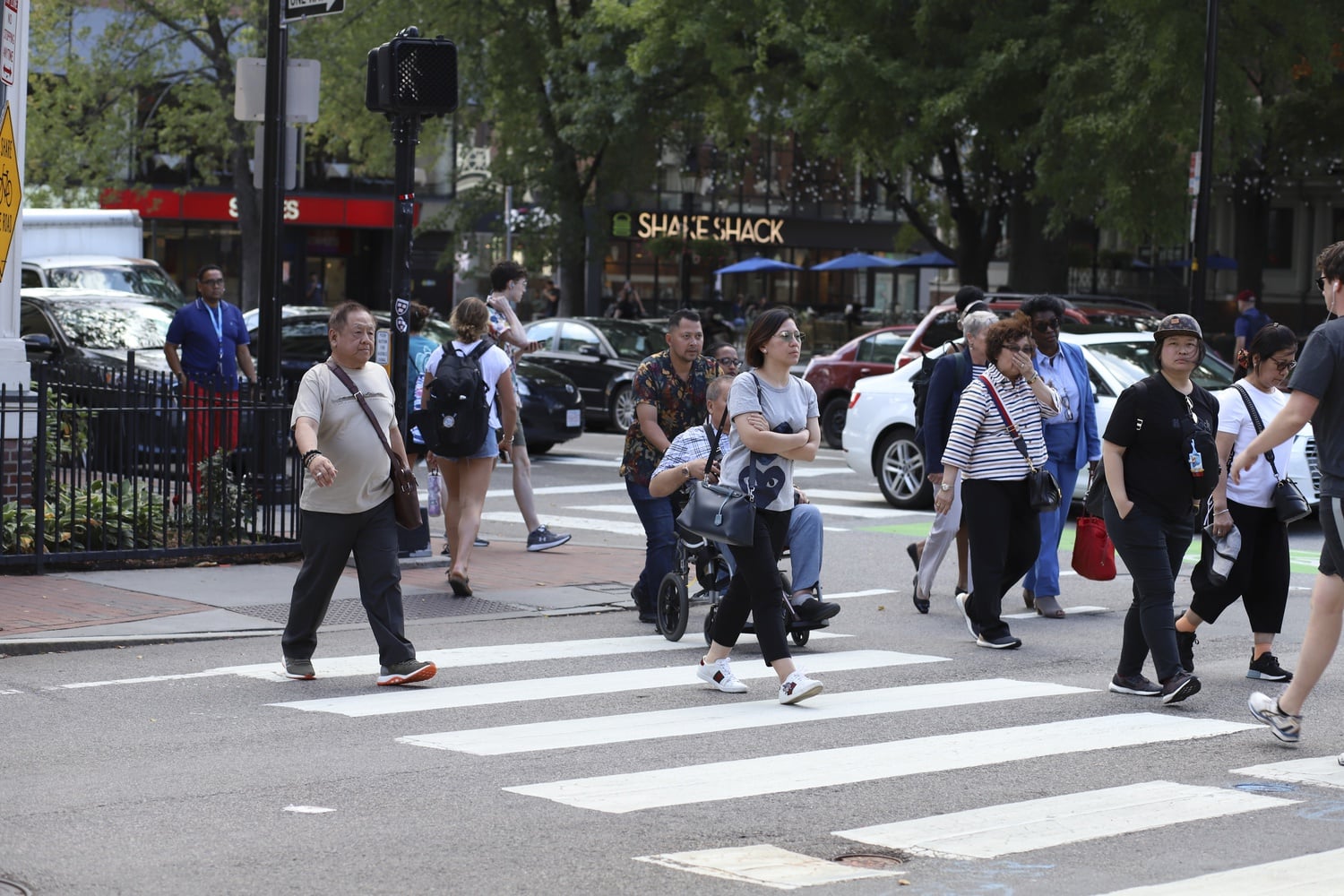 Pedestrians cross Massachusetts Avenue in groups, causing automobile traffic to stall for a moment.
