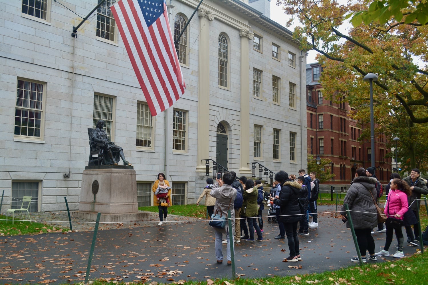 Tourists take photos of the John Harvard statue in front of University Hall.