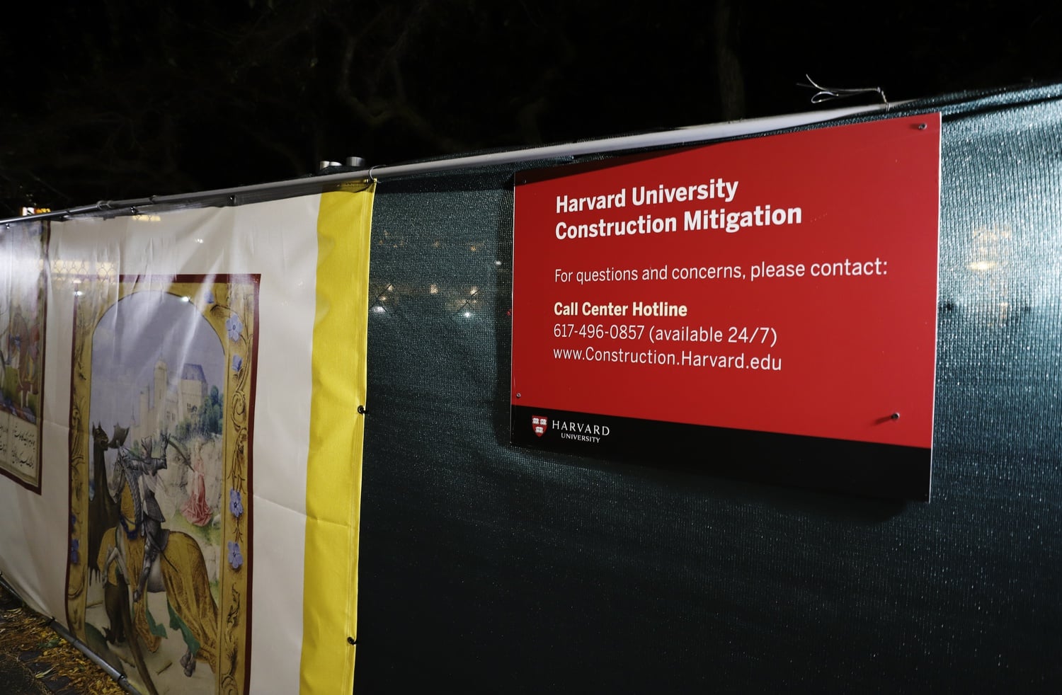 A construction mitigation sign hangs on a fence outside the Houghton Library construction site in Harvard Yard.