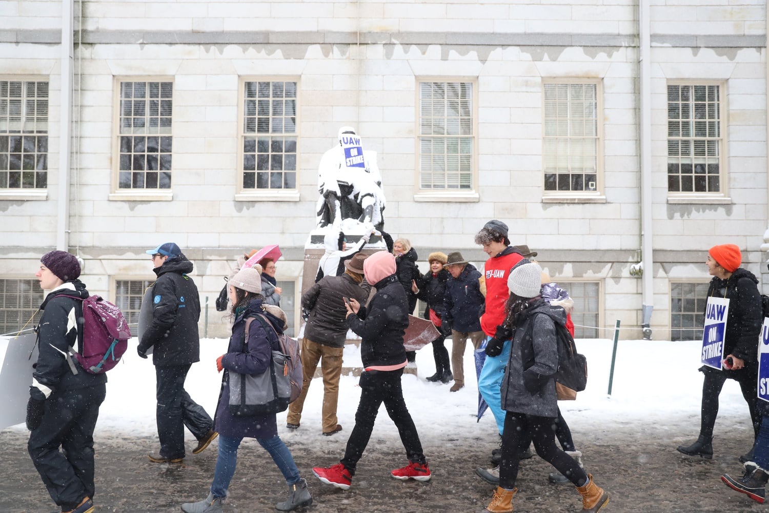Strikers march past the John Harvard Statue, which bears a sign supporting the union.