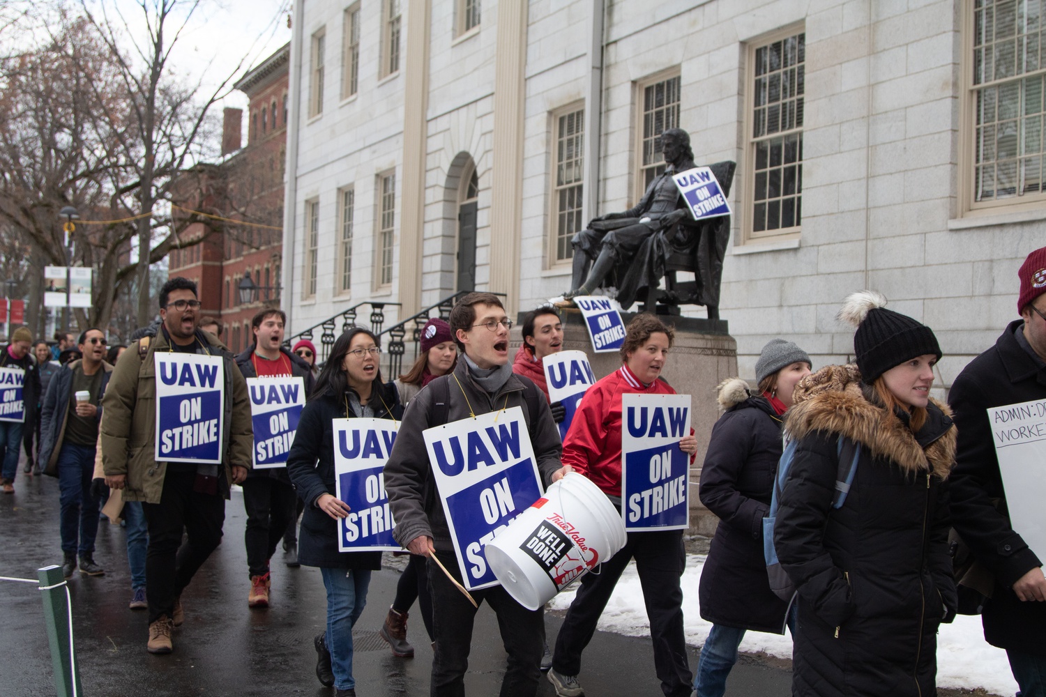 Members of Harvard Graduate Students Union-United Automobile Workers marched past the John Harvard statue bearing buckets and UAW signs.