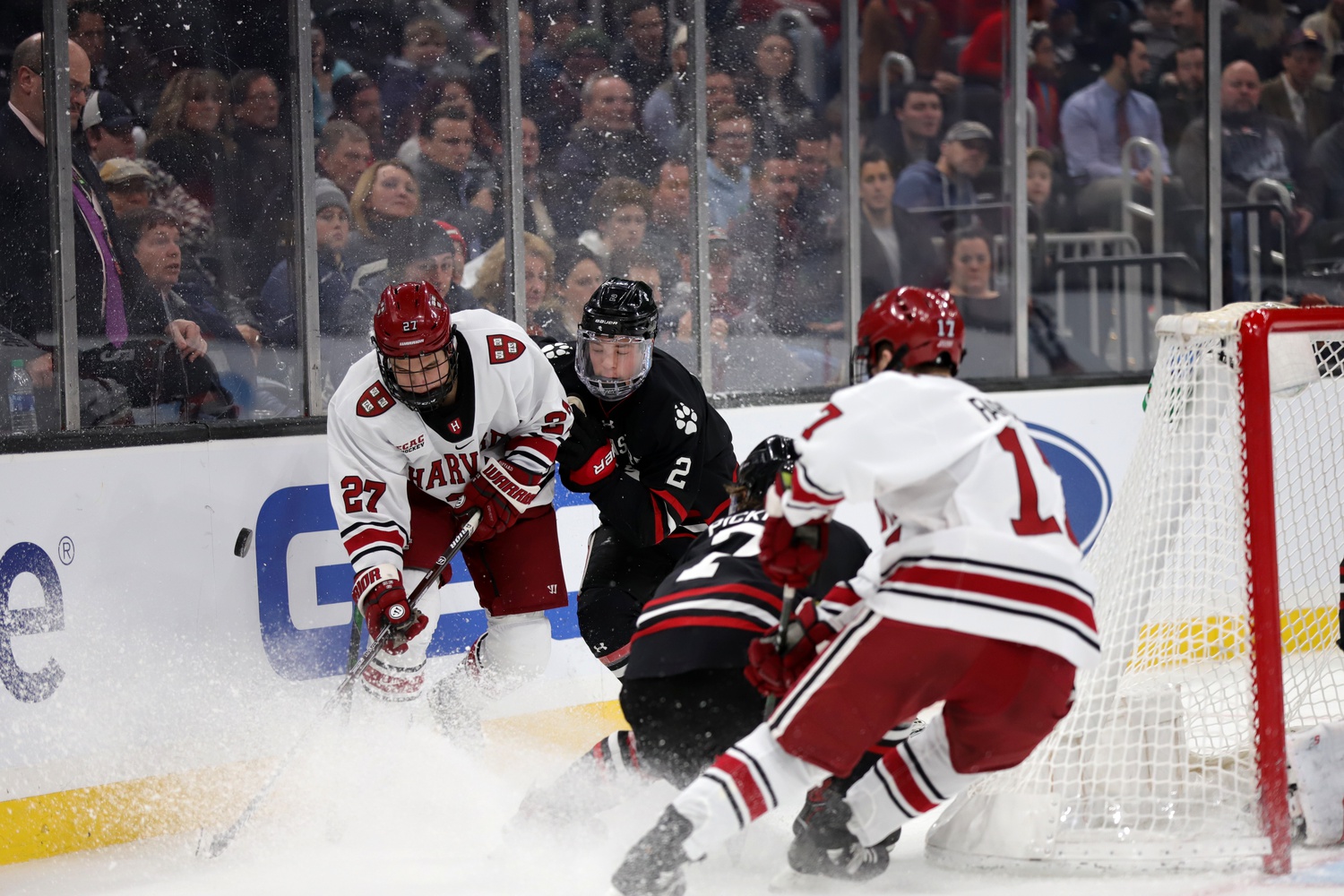 First-year forward Austin Wong of Harvard fights to maintain possession behind the net amid pressure from Huskies sophomore defenseman Jordan Harris.