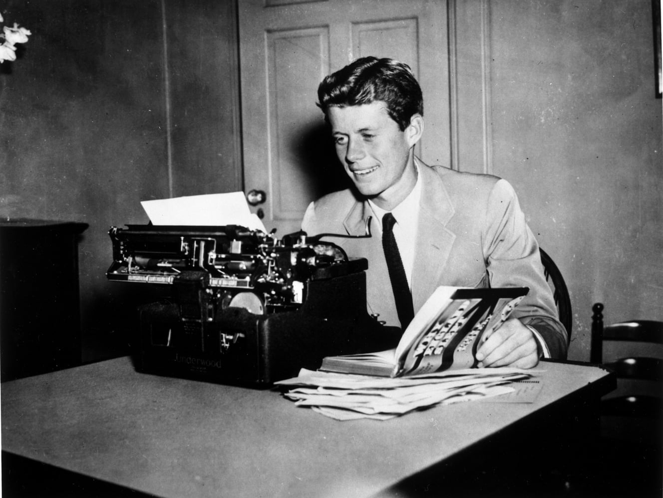 President John F. Kennedy ‘40 sits at a typewriter with his book “Why England Slept,” the published version of Kennedy’s thesis written in his senior year at Harvard College.