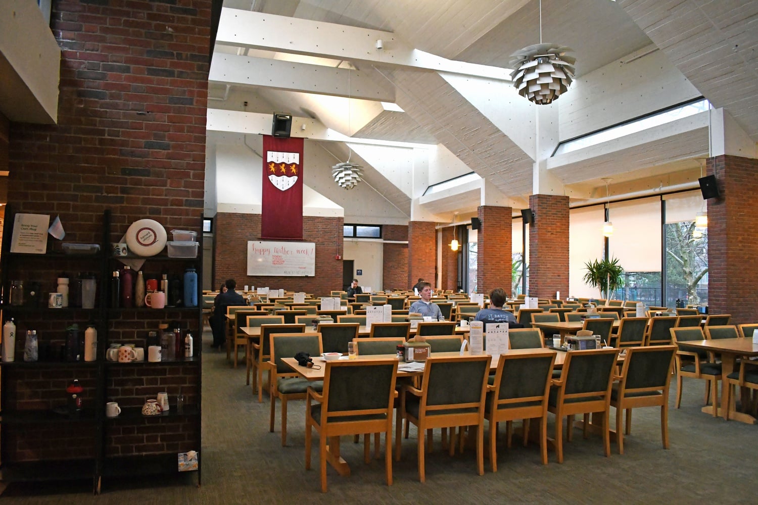 Students sit in the Mather House dining hall in 2020. Copies of an old edition of the Gorilla Gazette, the House's satire newsletter, are displayed in plastic stands on the tables.