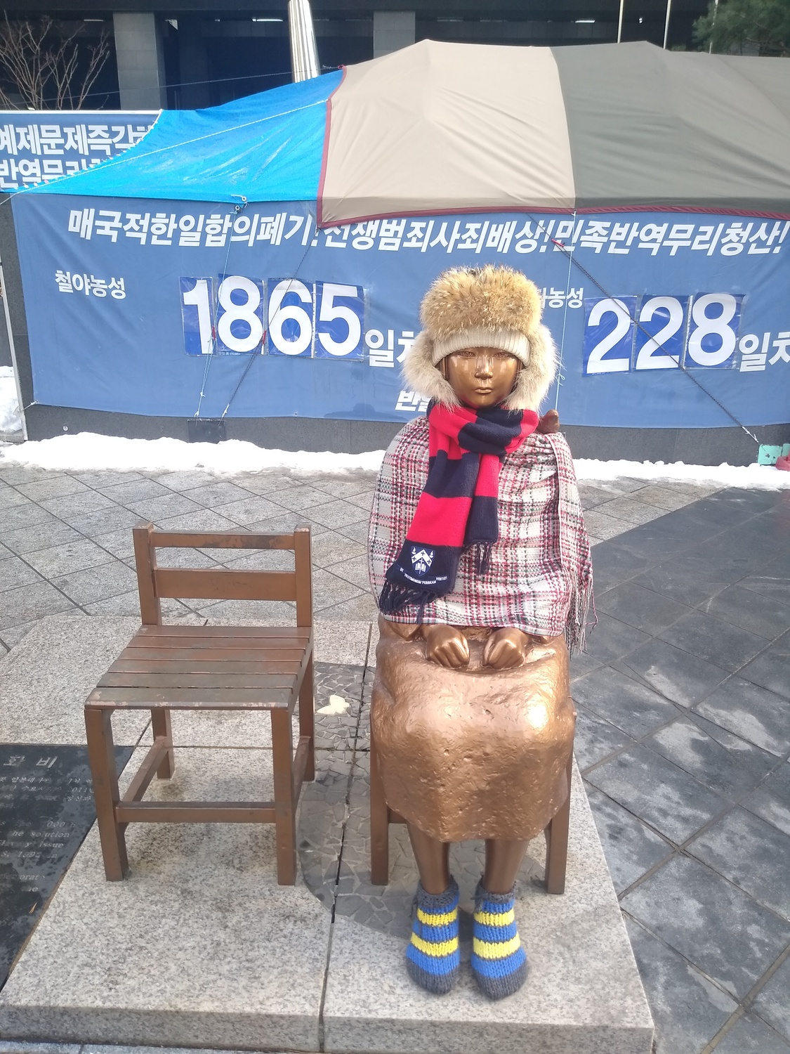 The Statue of Peace in front of the former Japanese Embassy in Seoul, South Korea commemorates comfort women, sex slaves taken by the Imperial Japanese Army during World War II. The slogans on the tarp behind the statue demand the Japanese government to make reparations.