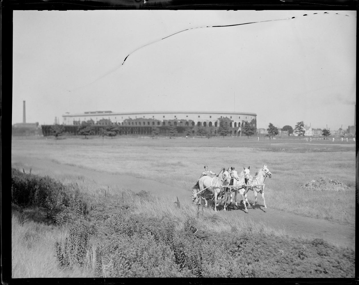 In a pre-World War II photograph, a chariot races along the former Charles River Speedway in Allston with Harvard Stadium in the distance. Much of this area of Allston was a former grassy marshland before it became an extension of Harvard campus.