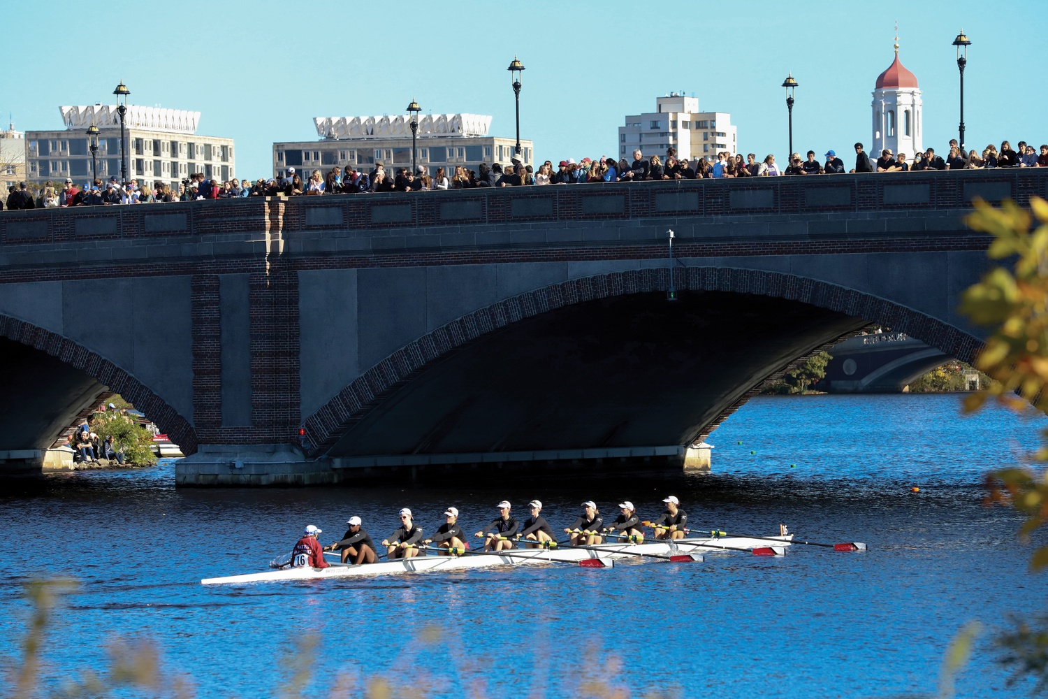 Crowds line a bridge to watch the action as a Bates College women’s eight passes by.
