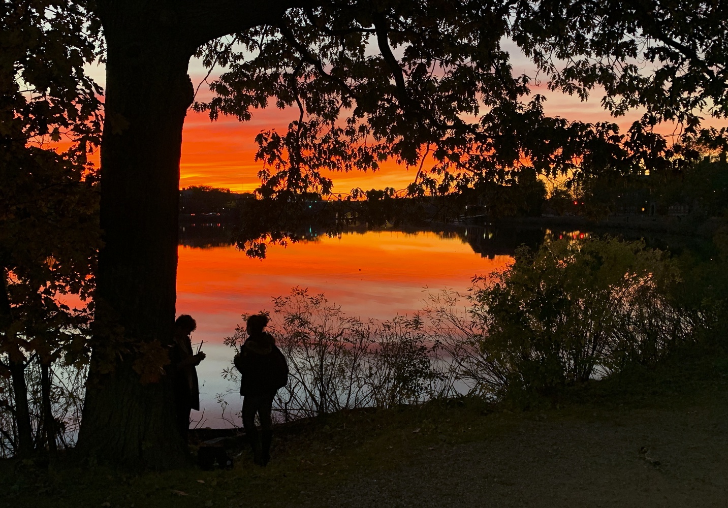 Two students take photos in front of a sunset over the Charles River Sunday evening.