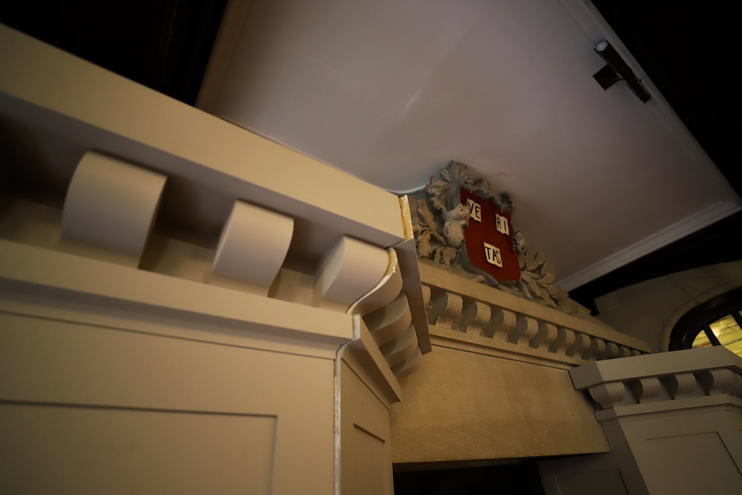 A large red Harvard shield on the overmantel of the Westmorly fireplace. The left pillar’s encasing seems to be cracked ajar.