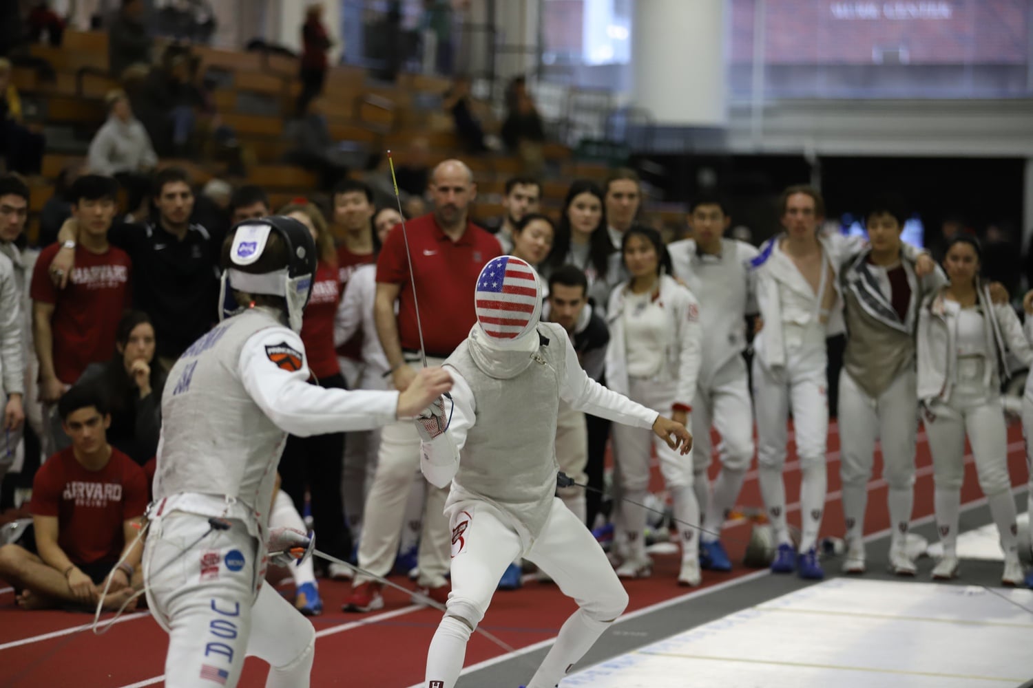 A Crimson fencer faces off against the Princeton Tigers at the Ivy League Championships in 2020 as teammates look on.