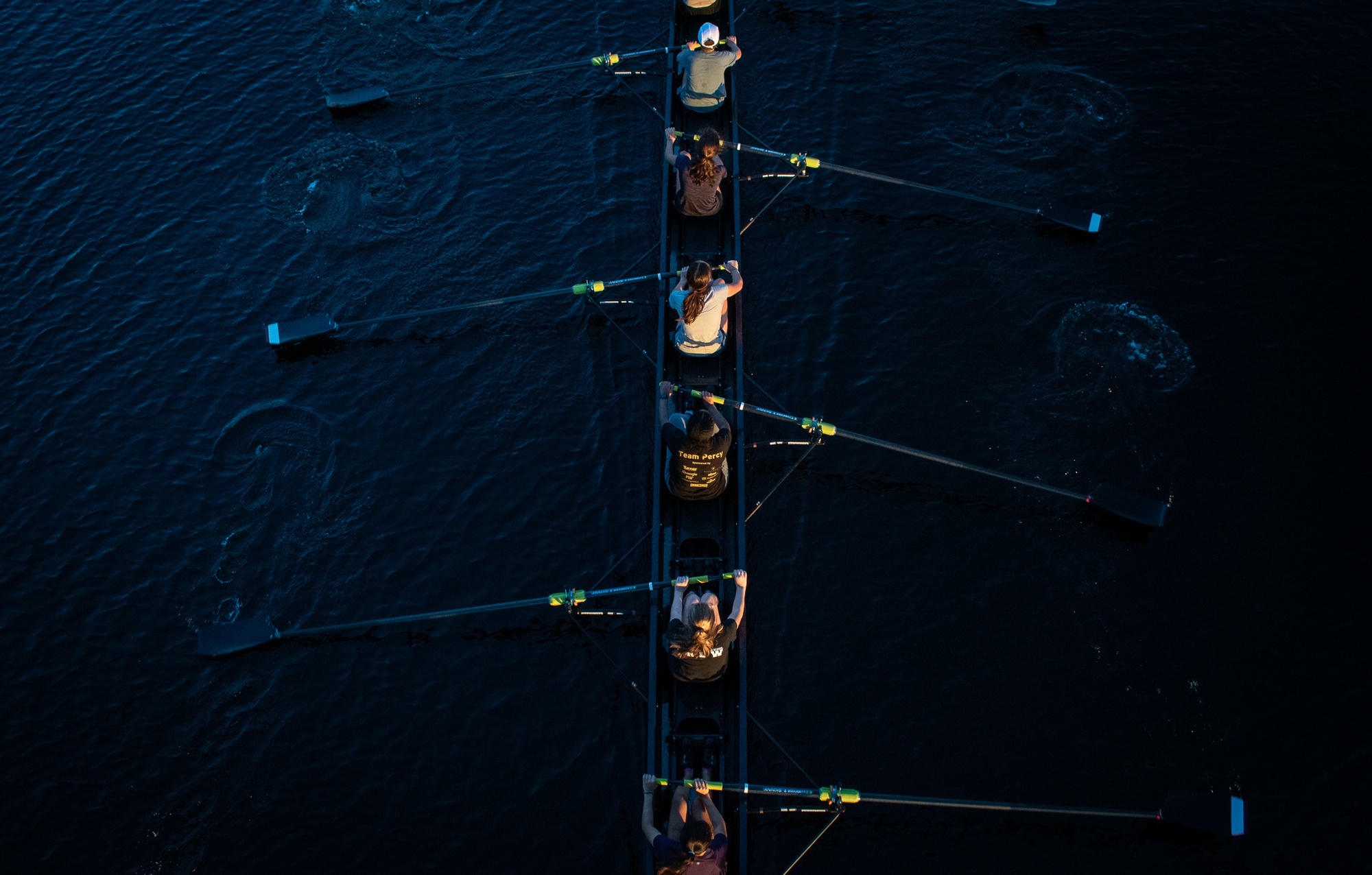 Members of the crew team row down the Charles, leaving ripples in their wake.