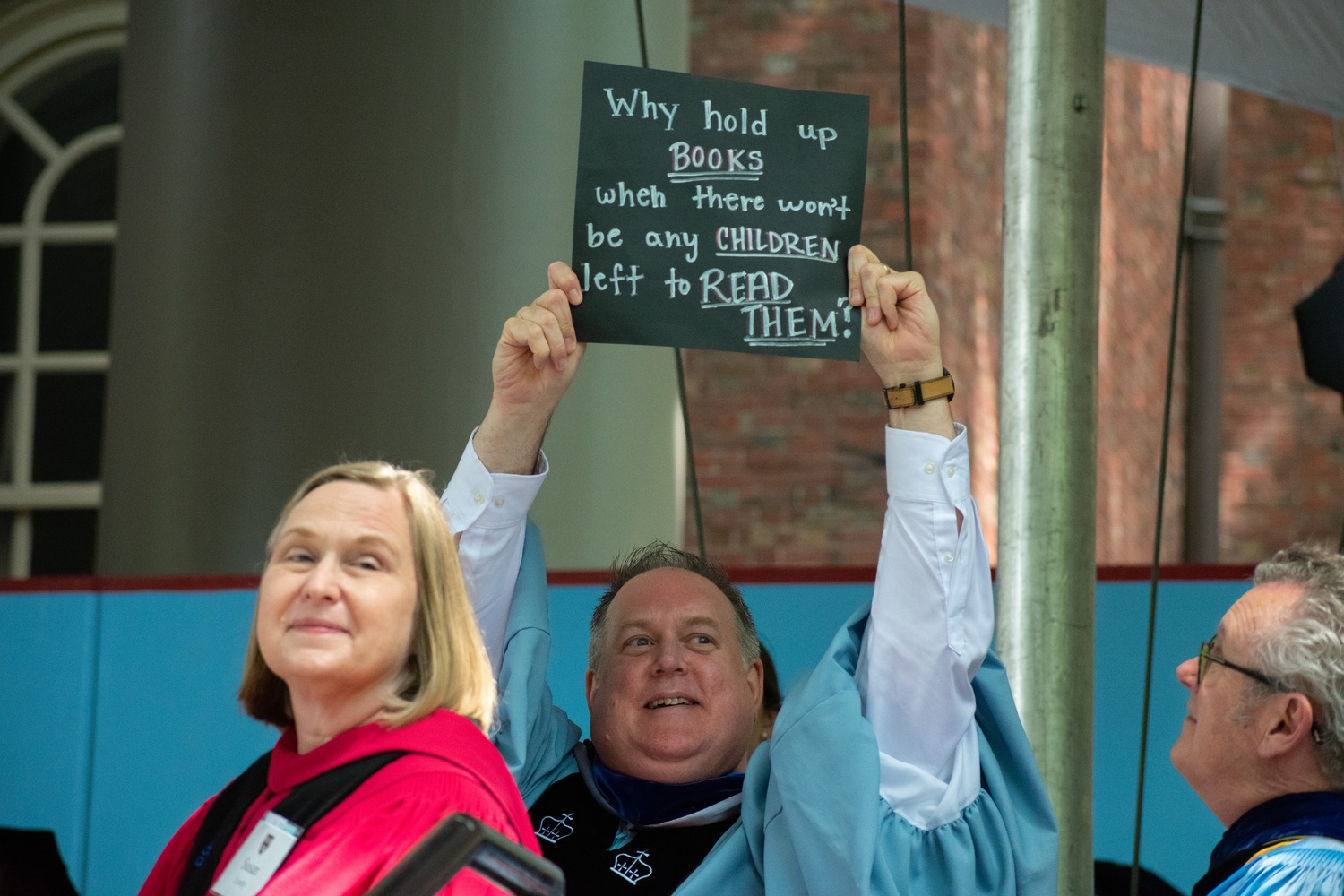 A man seated behind the podium at Thursday's Commencement Exercises held up a poster as Harvard Graduate School of Education students were conferred their degrees.
